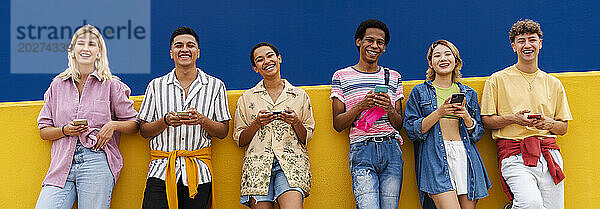 Group of friends leaning against yellow wall using their smartphones