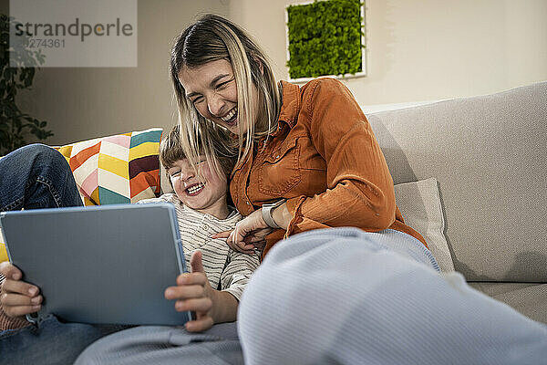 Fröhlicher Junge mit Mutter  die zu Hause einen Tablet-PC nutzt