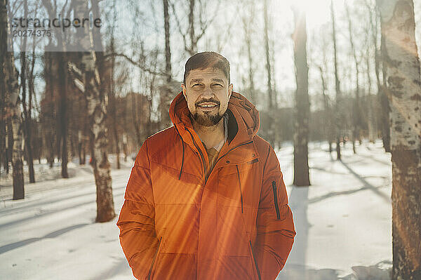 Lächelnder Mann mit orangefarbenem Mantel im Winter im Park