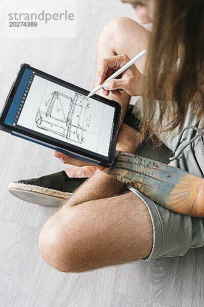 Junger Mann zeichnet auf Tablet-PC einen Bauplan für ein neues Zuhause