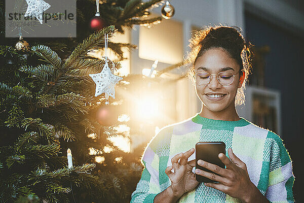 Frau benutzt Smartphone und steht neben Weihnachtsbaum