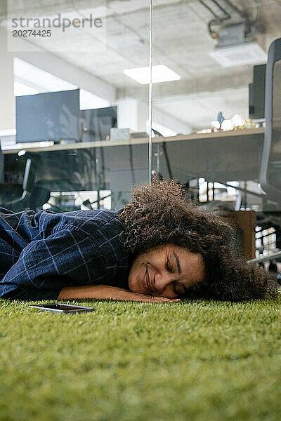 Lächelnde Geschäftsfrau  die im Büro auf dem Teppich liegt