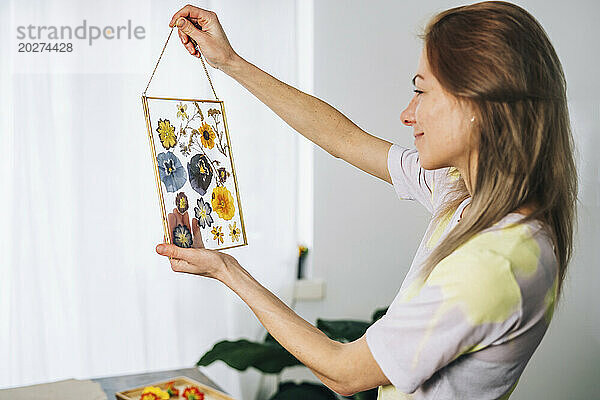 Woman holding transparent frame decorated with dried flowers at home