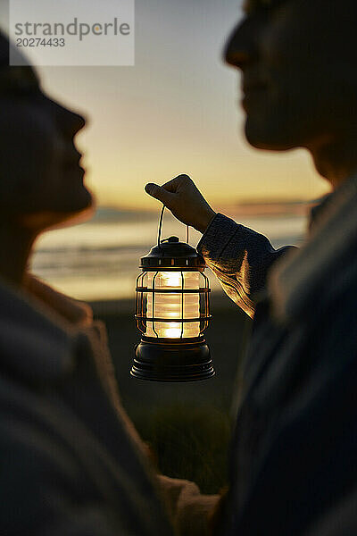Young man holding lantern and looking at woman on beach