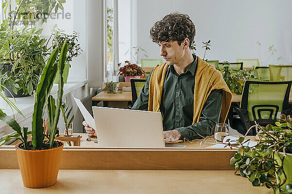 Geschäftsmann liest Dokumente neben Laptop im Büro