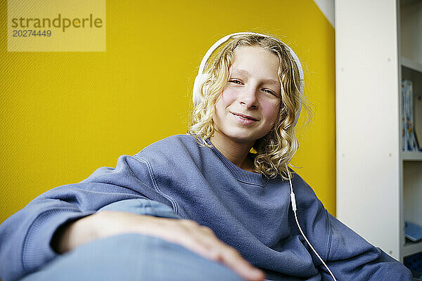 Smiling boy listening to music through headphones at home