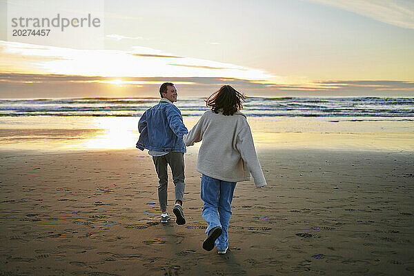 Freund hält Hand seiner Freundin und rennt am Strand in Richtung Meer