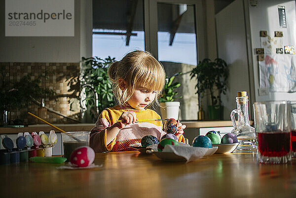 Cute girl decorating eggs for Easter at home