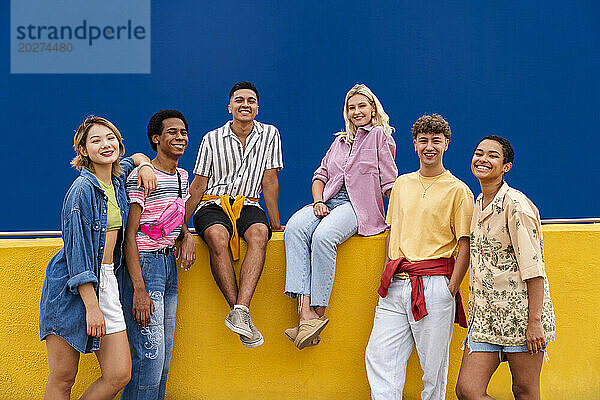 Eine Gruppe von Freunden mit farbenfroher Kleidung sitzt auf einer gelben Wand und unterhält sich