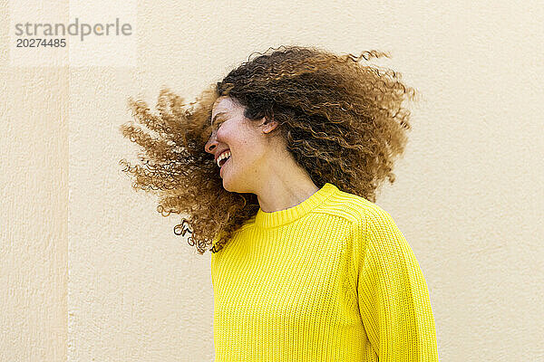 Cheerful woman tossing hair in front of wall