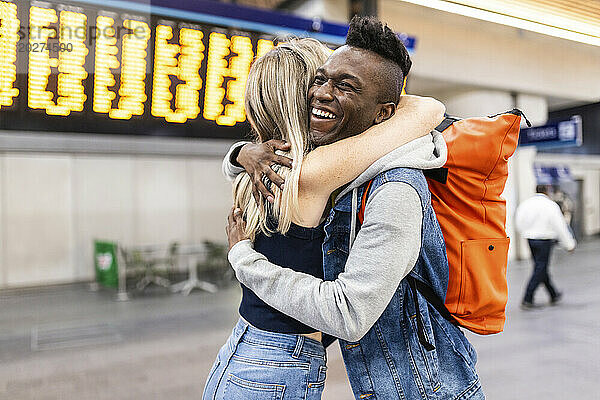 Smiling man embracing woman before departure at station