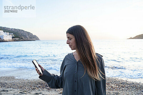 Frau benutzt Smartphone bei Sonnenuntergang am Strand