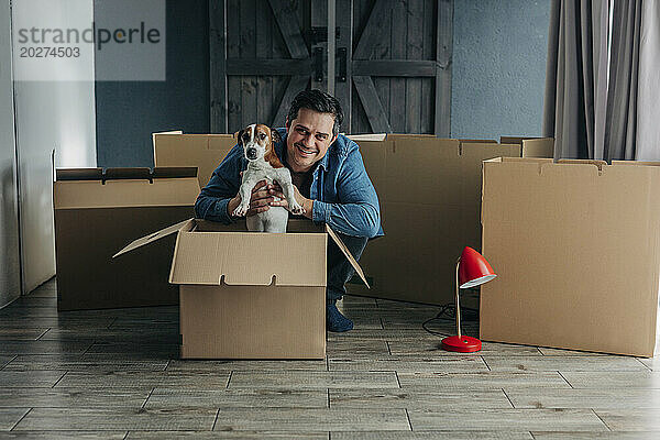 Glücklicher Mann mit Hund in der Nähe von Kartons zu Hause