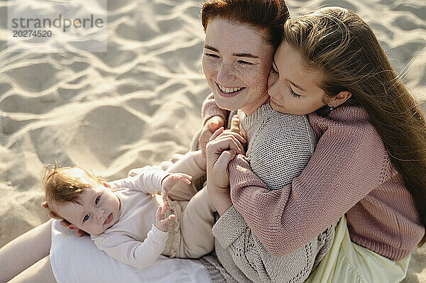 Glückliche Frau sitzt mit Töchtern am Strand