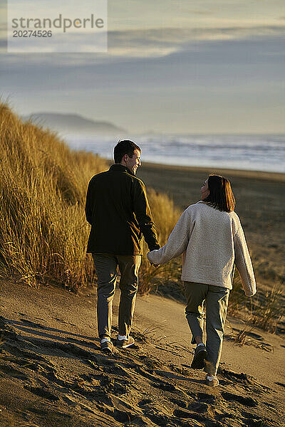 Junger Mann und Frau halten Händchen am Strand