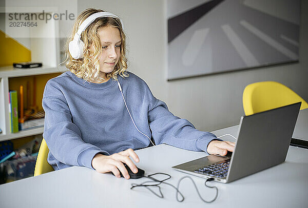 Boy wearing headphones and playing video game on laptop at home