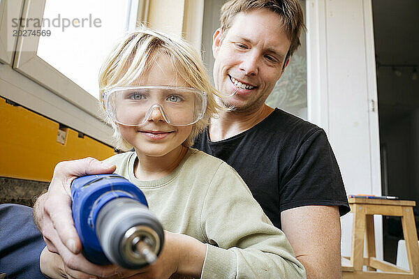 Lächelnder Sohn und Vater halten Bohrmaschine zu Hause