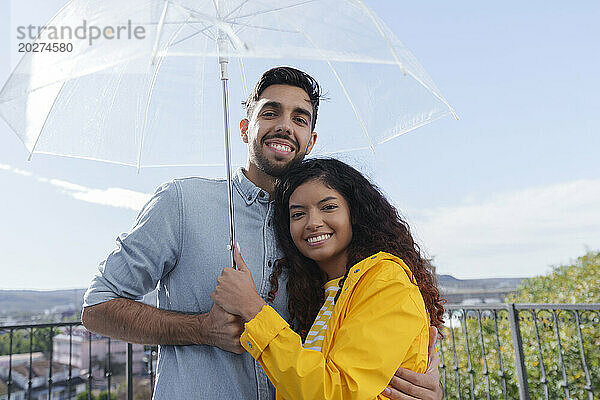 Glückliches Paar  das an einem sonnigen Tag unter einem Sonnenschirm auf dem Balkon steht