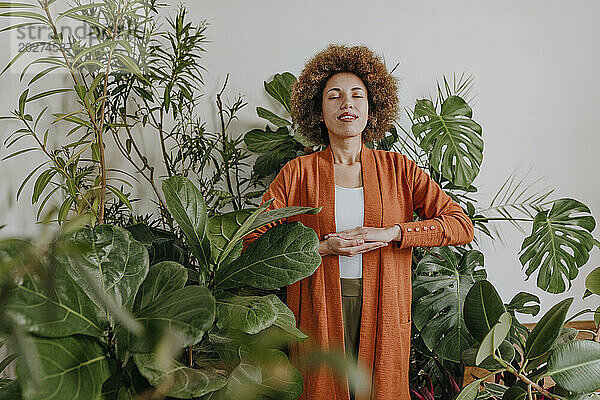 Glückliche Frau steht mit gefalteten Händen neben Pflanzen
