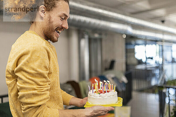 Glücklicher Geschäftsmann hält beleuchtete Geburtstagstorte im Büro