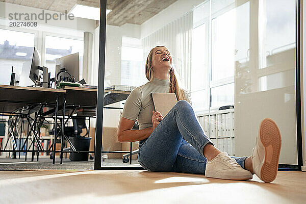 Fröhliche Geschäftsfrau sitzt mit Tablet-PC im Büro