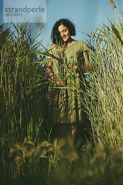 Lächelnde reife Frau  die inmitten von hohem Gras auf dem Feld steht