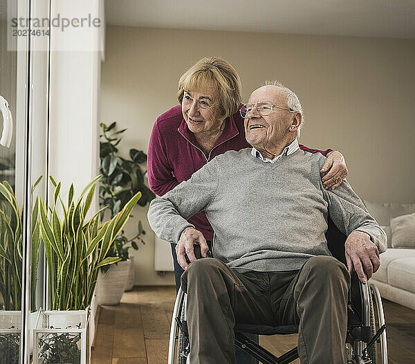 Glückliche ältere Frau  die sich um einen Mann kümmert  der im Rollstuhl sitzt