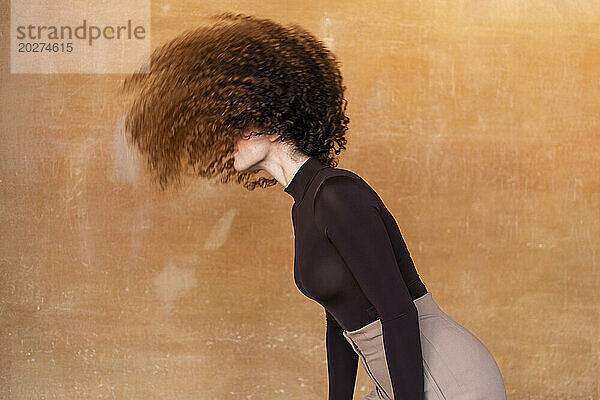 Junge Frau wirft Haare vor braunem Hintergrund