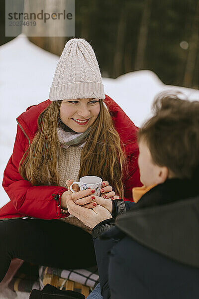 Lächelnde Frau hält im Winter eine Teetasse mit ihrem Freund