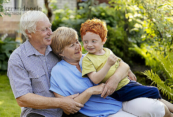 Lächelnder Junge sitzt mit Großeltern im Garten