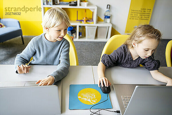 Jungen und Mädchen sitzen am Schreibtisch mit Laptops und lernen Computer im Klassenzimmer