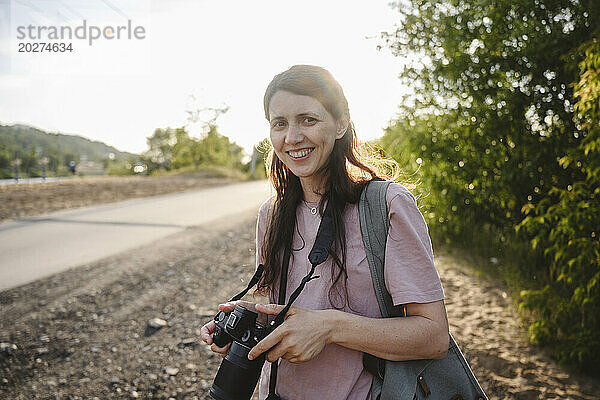 Lächelnde Frau hält Kamera an sonnigem Tag