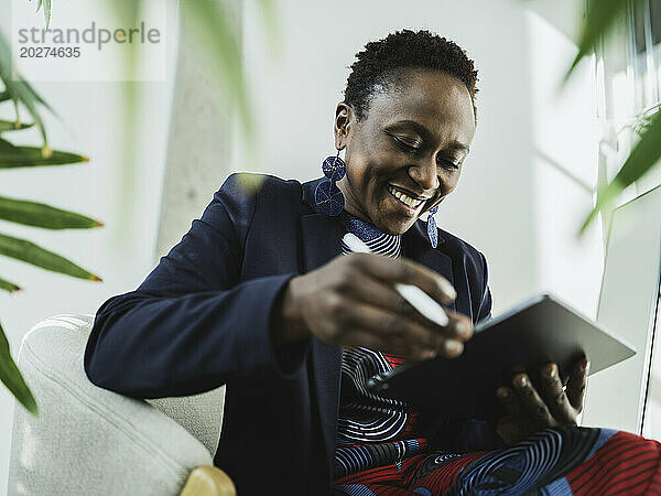 Lächelnde Geschäftsfrau blickt im Büro auf den Tablet-PC