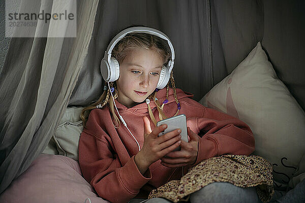 Girl wearing headphones using mobile phone in canopy at home