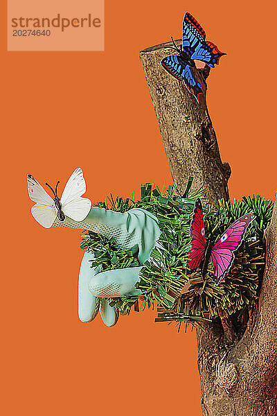 Artificial butterflies sitting on grass and tree trunk against orange background