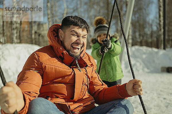 Cheerful father sitting on swing with son at park