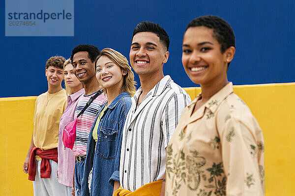 Eine multiethnische Gruppe junger Freunde steht lächelnd vor einer bunten Wand