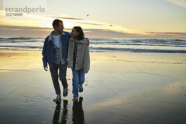 Lächelnder Mann und Frau gehen gemeinsam am Meeresstrand spazieren