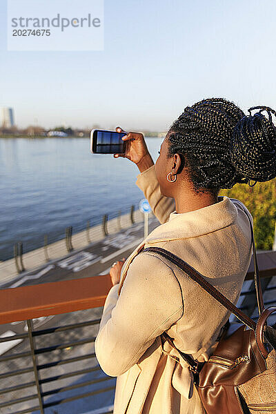 Frau fotografiert den Fluss bei Sonnenuntergang mit dem Handy