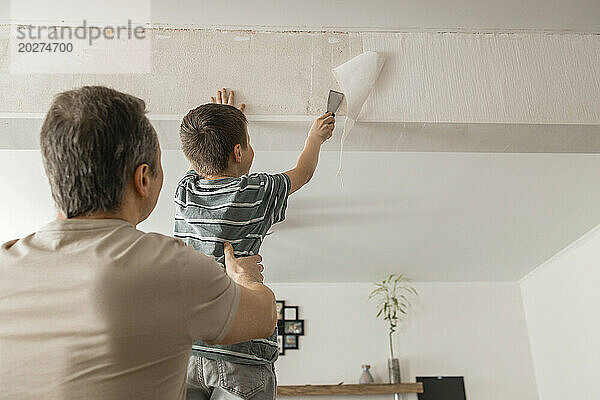 Sohn und Vater schälen zu Hause alte Tapeten mit Spachtel von der Wand