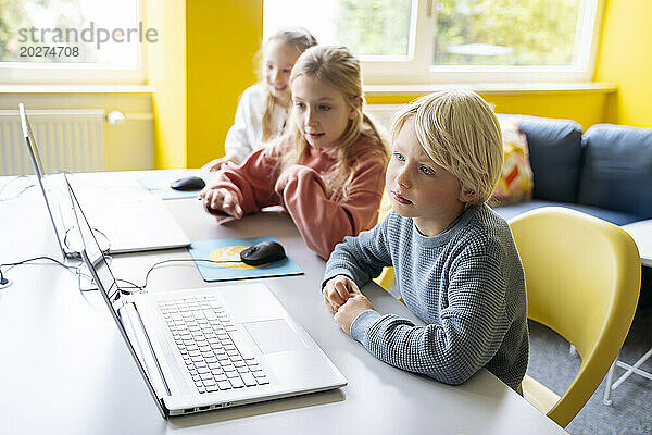 Blonder Junge sitzt mit Mädchen und lernt im Computerklassenzimmer