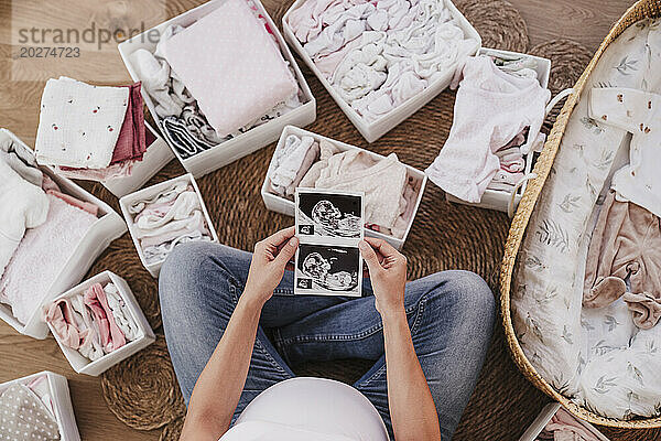 Schwangere Frau sitzt auf dem Boden und hält zu Hause Ultraschallbilder in der Hand