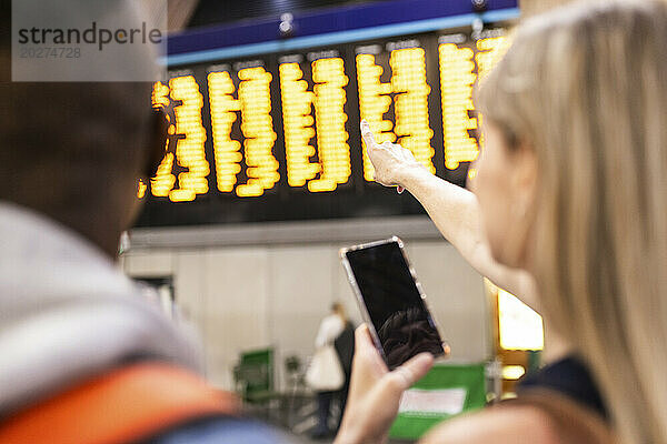 Frau überprüft den Fahrplan des Zuges und hält ihr Smartphone am Bahnhof in der Hand