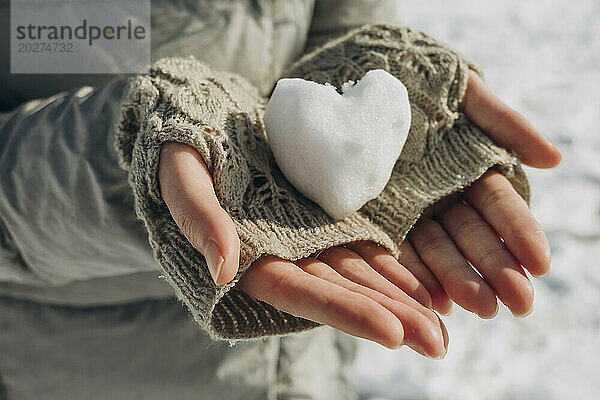 Frau hält herzförmigen Schneeball in der Hand