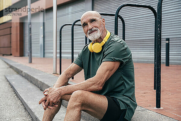 Älterer Mann mit kabellosen Kopfhörern sitzt auf Stufen