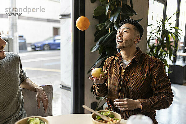 Geschäftsmann spielt mit Apfel und Orange im Bürocafé