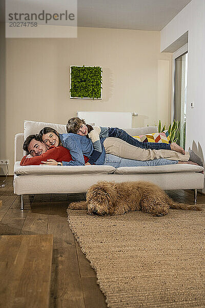 Happy father and mother lying on sofa near dog at home