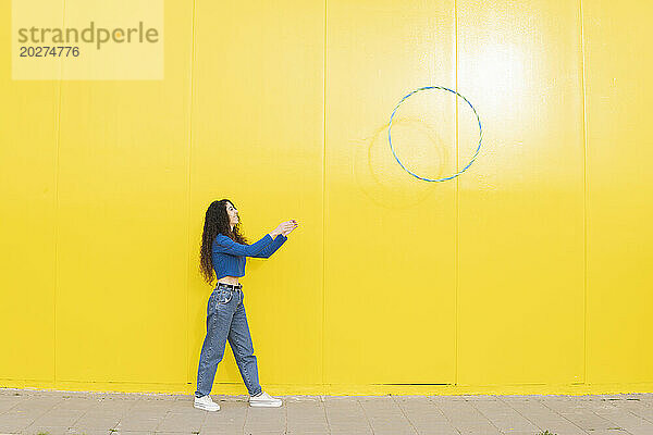 Woman throwing hula hoop standing against yellow background
