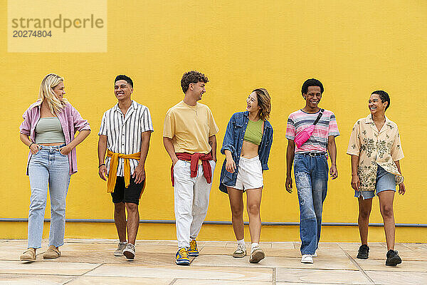 Multiethnische Gruppe junger Freunde  die Seite an Seite vor einer gelben Wand gehen