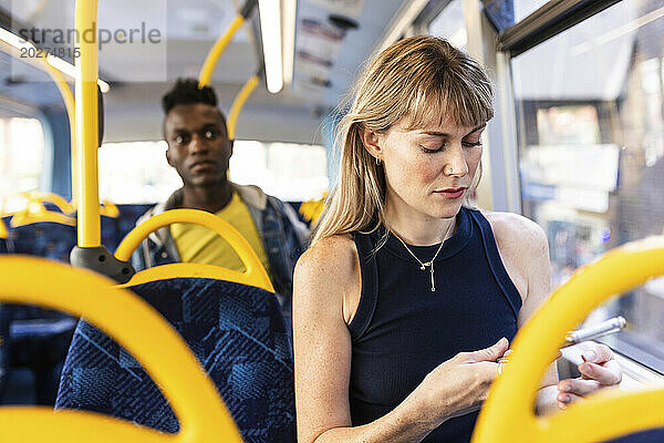 Frau benutzt Smartphone und sitzt mit Freundin im Bus